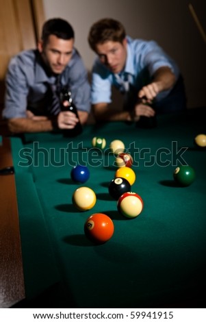 Two young men discussing snooker game at table, having beer, focus on snooker balls.?