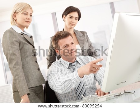 Business team in office, businessman pointing at computer, businesswomen looking at screen.?