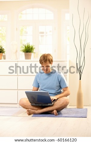 Young guy looking at laptop computer sitting on floor at home. ?