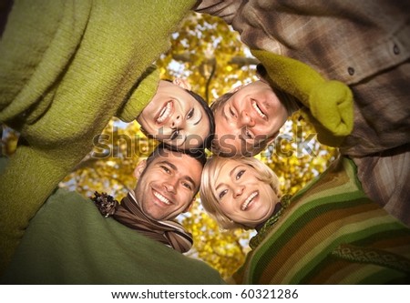 Group of happy friends standing with their heads together in autumn forest, smiling. Low angle view.?