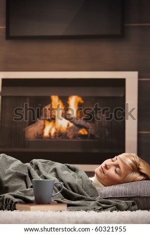 Woman sleeping at home lying on floor in front of a fire place,