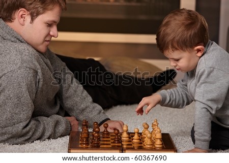 Father and 4 years old child playing chess at home in a cold winter day.