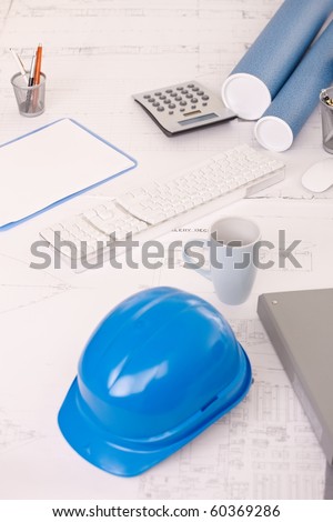 Desk in architect office, with design plan, hardhat, coffee mug, calculator and notes.?