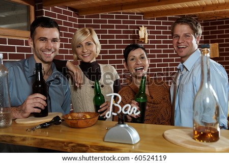 Happy young people standing at bar in pub, drinking beer, looking at camera, smiling.?