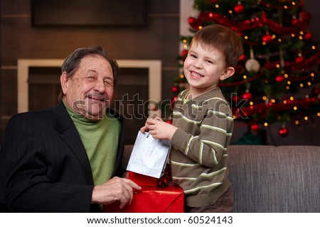 Young boy giving christmas present to happy grandfather, smiling. ?