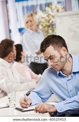 Young businessman sitting at table in office meeting room writing business notes.?