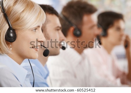 Four young customer service operators sitting in a row and talking on headset.?