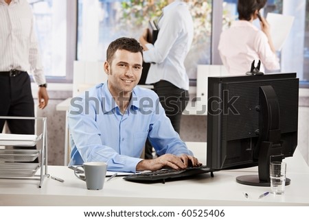 Casual businessman working with computer in office, looking at camera, smiling.?