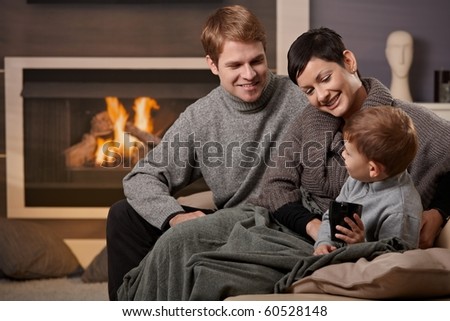 Happy family sitting on couch at home in front of fireplace, smiling.
