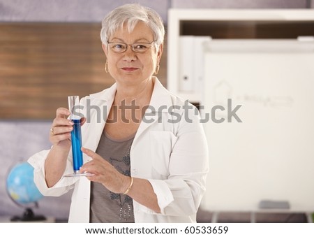 Senior teacher standing in classroom, holding test tube, teaching chemistry in elementary school.?