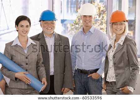 Happy designer team wearing hardhat in office holding architectural plan, smiling.?