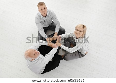 Three businesspeople in smart clothes meditating on floor, concentrating on team force, smiling at camera, overhead view.?