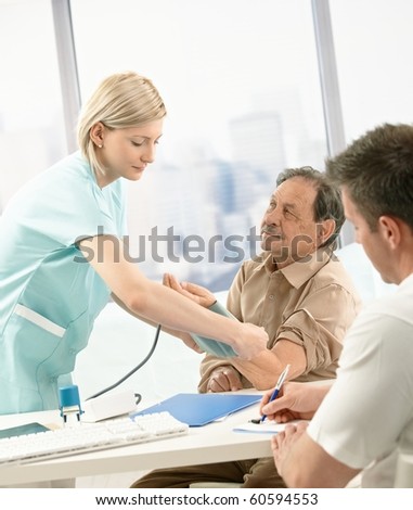 Nurse measuring blood pressure of old patient, doctor taking notes at desk.?