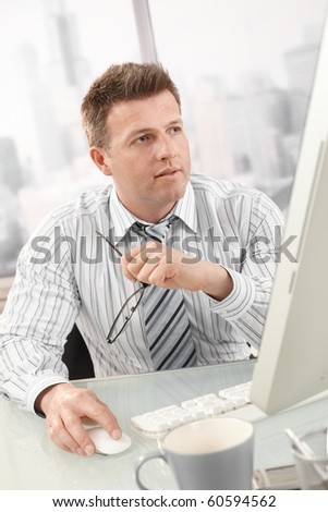 Businessman busy working with computer in office, holding glasses, looking at screen.?