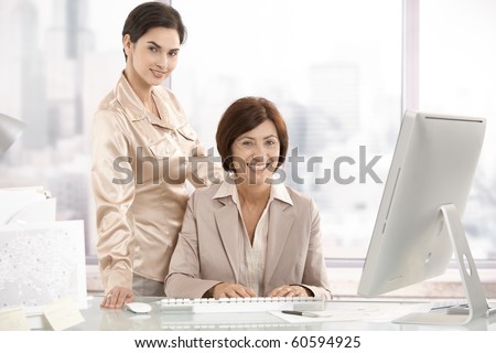 Portrait of senior executive woman with assistant in office, looking at camera, smiling.?
