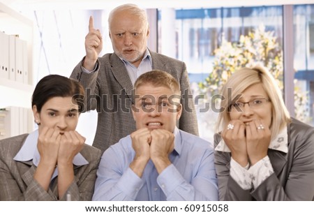 Angry boss shouting and pointing at scared employees in office.?
