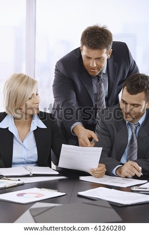 Business people reviewing documents in office, businessman pointing at paper, smiling.?