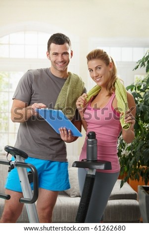 Young woman checking training plan with her personal trainer standing beside exercise bike at home.
