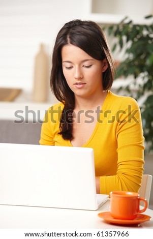 Beautiful teen girl learning with laptop computer sitting at table with mug.