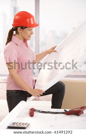 Female architect working in office, looking at rolled out floor plan, smiling.?
