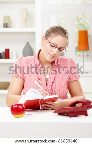 Happy young woman sitting at table writing in diary book, smiling.