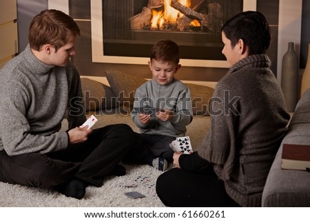 Young family with 4 years old kid playing card game at home in a cold winter day.