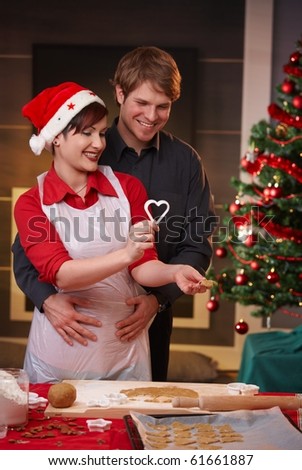Happy woman baking christmas cake, man embracing her, smiling.?