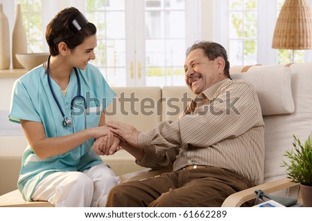 Happy nurse holding hands of elderly patient sitting side by side at home, laughing.?