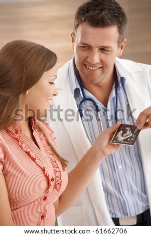 Smiling doctor showing pregant woman ultrasound picture of baby.?