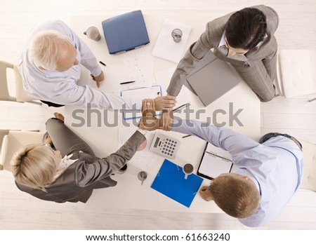 Businesspeople holding hands united over meeting table, while teamworking, high angle view.?