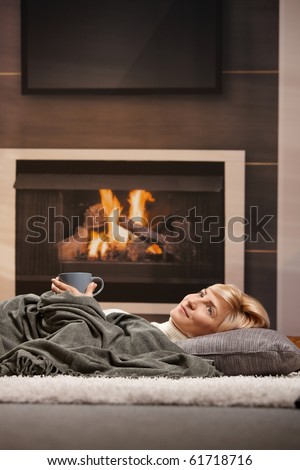 Woman resting at home lying on floor in front of a fire place,