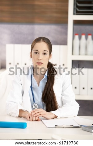 Portrait of female medical doctor sitting at desk in doctors office looking at camera. Copyspace above.?