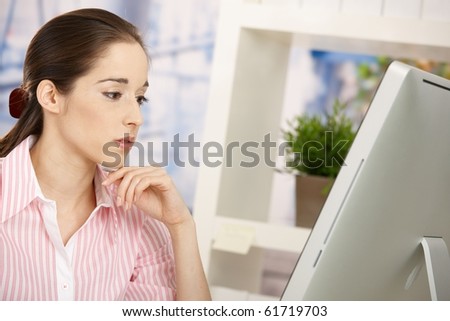 Pretty girl in office busy working on computer, looking at screen, thinking.?
