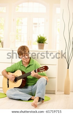 Goodlooking guy playing guitar in bright living room.?