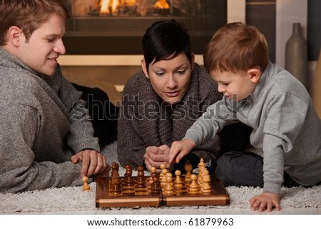 Young family with 4 years old kid playing chess at home in a cold winter day.