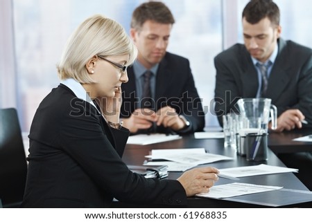 Serious businesswoman talking on phone at meeting with businessmen in background.?