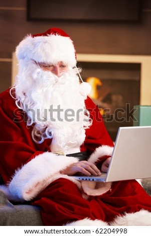 Modern Santa Claus sitting by fireplace using computer computer.?
