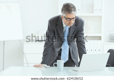 Gray haired executive businessman working on laptop computer at desk, in office.