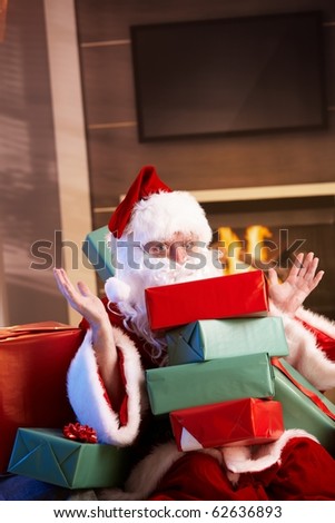 Portrait of Santa Claus sitting by fireplace holding a pile of Christmas presents.?