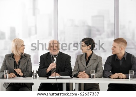 Businessteam on meeting, senior executive talking into microphone giving speech, smiling.?