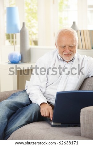 Cheerful pensioner using laptop computer on couch, looking at screen, smiling.?