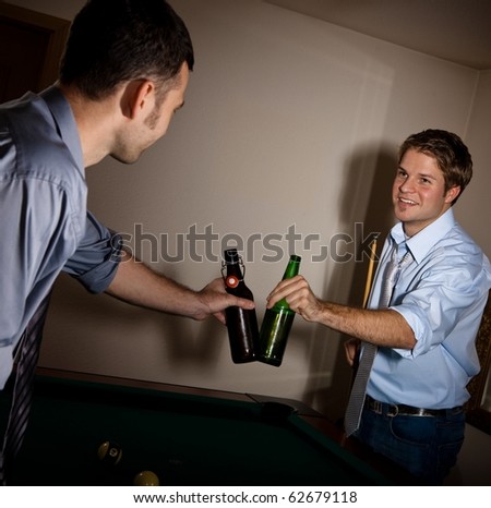 Young handsome men clinking beer bottles at snooker, smiling at each other, celebrating game.?