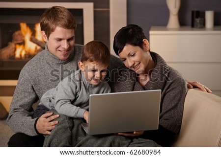 Happy family sitting on couch at home in winter, using laptop computer, smiling.