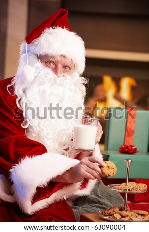 Satisfied Santa Claus sitting at fireplace drinking milk and eating chocolate chip cookies, looking at camera.?