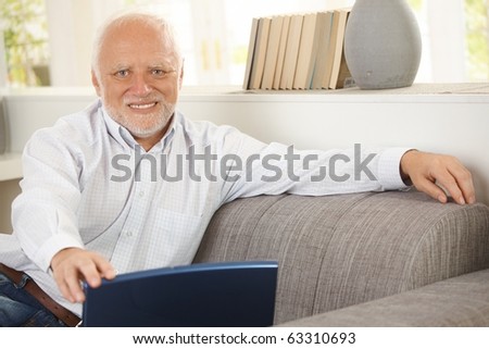 Portrait of elderly man sitting on sofa, holding laptop computer, smiling happily at camera.?