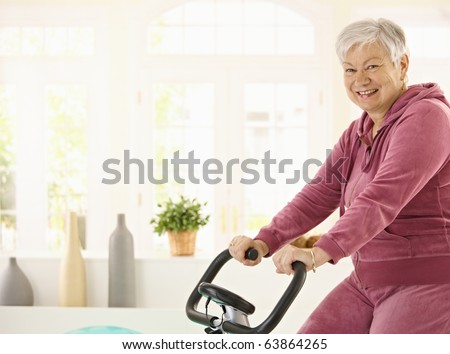 Healthy elderly woman training at home with exercise bike, smiling.?