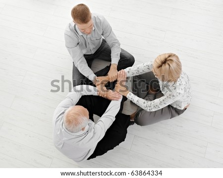 Three businesspeople meditating together, holding hands, expressing team spirit, sitting on floor, high angle view.?