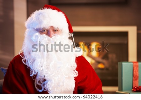 Indoor portrait of Santa Claus sitting by fireplace, looking at camera.?