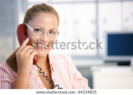 Pretty receptionist working in office, talking on phone, smiling.?