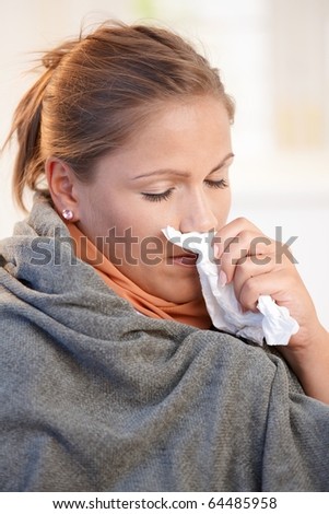 Young woman caught cold, feeling bad, blowing her nose, wrapped up in blanket.?
